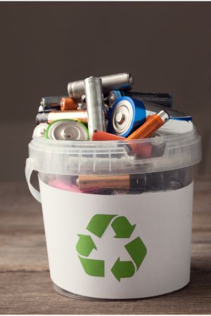 different sizes of batteries in a white bucket with a recycling icon on it